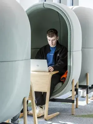 A male student works from his laptop in a one-person study pod.